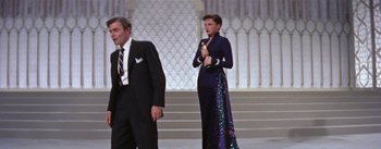 Movie still from “A Star Is Born” (1954), directed by George Cukor – A man and a woman standing next to each other holding an award; Wide shot, Low angle