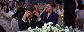 Movie still from “A Star Is Born” (1954), directed by George Cukor – A man and a woman sitting in front of a table; Medium shot, High angle