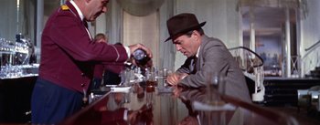 Movie still from “A Star Is Born” (1954), directed by George Cukor – A man in a hat is sitting at a table drinking a shot; Medium shot, Over the shoulder angle