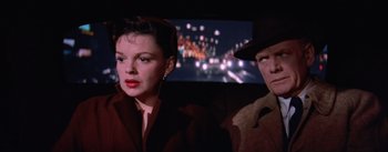 Movie still from “A Star Is Born” (1954), directed by George Cukor – A man and a woman sitting next to each other in a car; Close Up shot, Over the shoulder angle