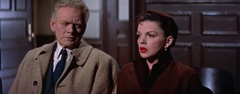Movie still from “A Star Is Born” (1954), directed by George Cukor – An older man and a younger woman standing next to each other in front of a door; Close Up shot, Low angle