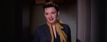 Movie still from “A Star Is Born” (1954), directed by George Cukor – A woman wearing a yellow neck scarf and a black jacket; Close Up shot, Low angle