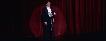 Movie still from “A Star Is Born” (1954), directed by George Cukor – A man in a tuxedo standing on a stage with microphones; Wide shot, Low angle