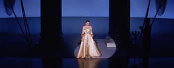 Movie still from “A Star Is Born” (1954), directed by George Cukor – A woman in a gold dress standing on a runway; Wide shot, Low angle