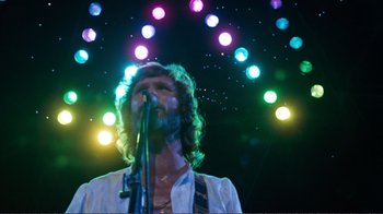 Movie still from “A Star Is Born” (1976), directed by Frank Pierson – A man with long hair is holding a microphone; Medium shot, Low angle