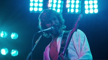 Movie still from “A Star Is Born” (1976), directed by Frank Pierson – A man holding a guitar and singing into a microphone; Medium shot, Low angle