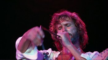 Movie still from “A Star Is Born” (1976), directed by Frank Pierson – A man with long hair and a beard is holding a microphone; Close Up shot, Low angle