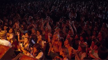 Movie still from “A Star Is Born” (1976), directed by Frank Pierson – A crowd of people sitting and standing in front of a microphone; Wide shot, High angle