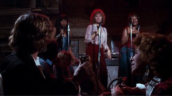 Movie still from “A Star Is Born” (1976), directed by Frank Pierson – A group of women singing into microphones in front of a crowd; Wide shot, Over the shoulder angle