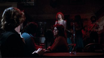Movie still from “A Star Is Born” (1976), directed by Frank Pierson – A group of people sitting at a table with microphones; Wide shot, Over the shoulder angle