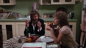 Movie still from “A Star Is Born” (1976), directed by Frank Pierson – A man and a woman sitting at a table eating pizza; Medium shot, High angle