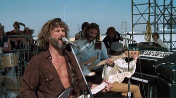 Movie still from “A Star Is Born” (1976), directed by Frank Pierson – A group of men playing instruments and singing; Medium shot, Low angle