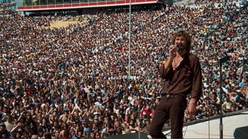 Movie still from “A Star Is Born” (1976), directed by Frank Pierson – A large crowd of people watching a man sing on a stage; Wide shot, High angle