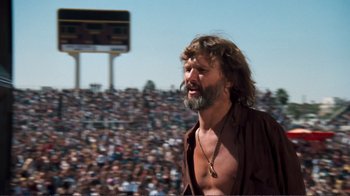 Movie still from “A Star Is Born” (1976), directed by Frank Pierson – A man with long hair and a beard standing in front of a crowd; Medium shot, Low angle
