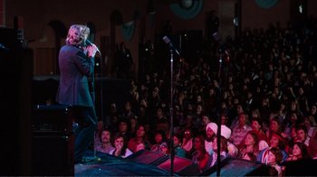 Movie still from “A Star Is Born” (1976), directed by Frank Pierson – A crowd of people watching a man sing on a stage with microphones and microphones; Wide shot, High angle