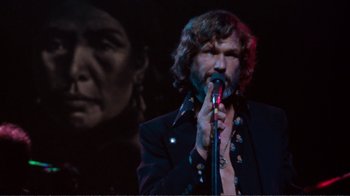Movie still from “A Star Is Born” (1976), directed by Frank Pierson – A man holding a microphone while standing next to a woman; Medium shot, Low angle
