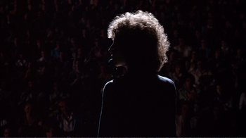 Movie still from “A Star Is Born” (1976), directed by Frank Pierson – A person with curly hair standing in front of an audience; Medium shot, Low angle