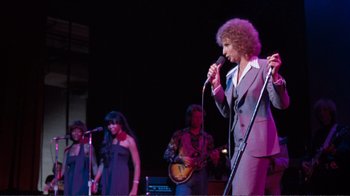 Movie still from “A Star Is Born” (1976), directed by Frank Pierson – A group of people on a stage with a microphone; Medium shot, Low angle
