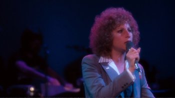Movie still from “A Star Is Born” (1976), directed by Frank Pierson – A woman with a curly hair is singing into a microphone; Close Up shot, High angle