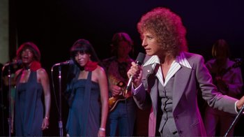 Movie still from “A Star Is Born” (1976), directed by Frank Pierson – A woman holding a microphone while standing next to a man; Medium shot, Low angle