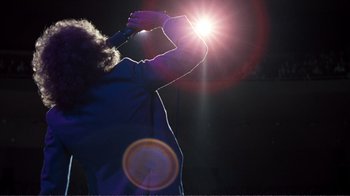 Movie still from “A Star Is Born” (1976), directed by Frank Pierson – A person holding a microphone up to a lens flare; Wide shot, Low angle