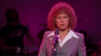 Movie still from “A Star Is Born” (1976), directed by Frank Pierson – A woman in a purple suit is holding a microphone; Medium shot, Over the shoulder angle