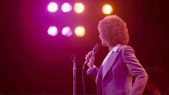 Movie still from “A Star Is Born” (1976), directed by Frank Pierson – A person holding a microphone on a stage; Medium shot, Low angle