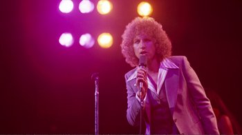 Movie still from “A Star Is Born” (1976), directed by Frank Pierson – A person with curly hair is holding a microphone; Medium shot, Low angle