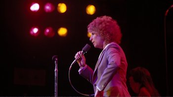 Movie still from “A Star Is Born” (1976), directed by Frank Pierson – A person holding a microphone on a stage; Medium shot, Low angle