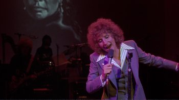 Movie still from “A Star Is Born” (1976), directed by Frank Pierson – A woman with curly hair is singing into a microphone; Medium shot, High angle
