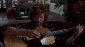 Movie still from “A Star Is Born” (1976), directed by Frank Pierson – A man with a beard is holding a guitar; Medium shot, Low angle