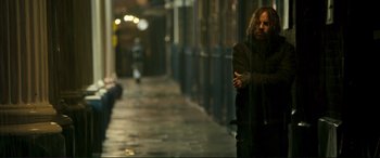 Movie still from “A Street Cat Named Bob” (2016), directed by Roger Spottiswoode – A man walking down a street at night with his arms crossed; Medium shot, Low angle