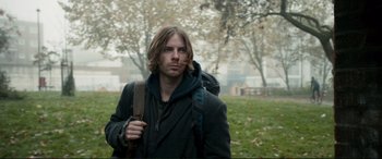 Movie still from “A Street Cat Named Bob” (2016), directed by Roger Spottiswoode – A man with long hair and a backpack in a park; Medium shot, Low angle