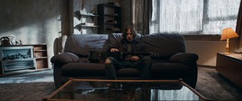 Movie still from “A Street Cat Named Bob” (2016), directed by Roger Spottiswoode – A man sitting on top of a couch holding a guitar; Wide shot, High angle