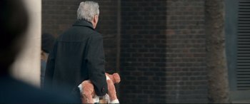 Movie still from “A Street Cat Named Bob” (2016), directed by Roger Spottiswoode – An older man holding a teddy bear in his arms; Medium shot, Over the shoulder angle