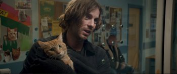 Movie still from “A Street Cat Named Bob” (2016), directed by Roger Spottiswoode – A man with long hair holding an orange cat; Close Up shot, Over the shoulder angle