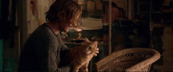 Movie still from “A Street Cat Named Bob” (2016), directed by Roger Spottiswoode – A person holding a cat in a room with wicker furniture; Medium shot, Over the shoulder angle