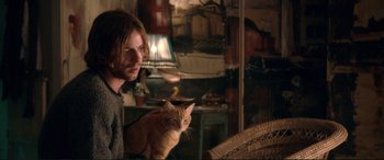 Movie still from “A Street Cat Named Bob” (2016), directed by Roger Spottiswoode – A man holding a cat while sitting on a chair; Medium shot, Over the shoulder angle