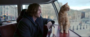 Movie still from “A Street Cat Named Bob” (2016), directed by Roger Spottiswoode – A man sitting in the back of a car next to a cat; Medium shot, Over the shoulder angle