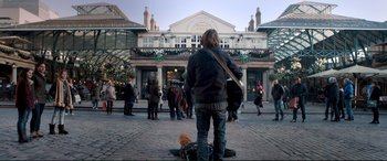 Movie still from “A Street Cat Named Bob” (2016), directed by Roger Spottiswoode – A man with a guitar stands on the street; Wide shot, Over the shoulder angle