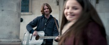 Movie still from “A Street Cat Named Bob” (2016), directed by Roger Spottiswoode – A man and a woman are playing a guitar together; Medium shot, Over the shoulder angle