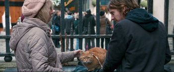 Movie still from “A Street Cat Named Bob” (2016), directed by Roger Spottiswoode – A man and woman petting a cat on a bench; Medium shot, Over the shoulder angle