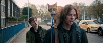Movie still from “A Street Cat Named Bob” (2016), directed by Roger Spottiswoode – A cat on a leash on a man's shoulder; Medium shot, Low angle