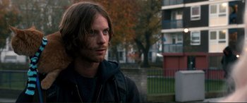 Movie still from “A Street Cat Named Bob” (2016), directed by Roger Spottiswoode – A man with long brown hair wearing a black jacket; Close Up shot, Over the shoulder angle
