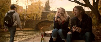 Movie still from “A Street Cat Named Bob” (2016), directed by Roger Spottiswoode – A woman sitting on a bench near a body of water; Medium shot, High angle