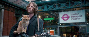 Movie still from “A Street Cat Named Bob” (2016), directed by Roger Spottiswoode – A man holding a guitar with a cat on his shoulder; Medium shot, Low angle