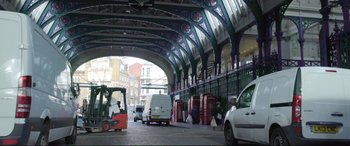 Movie still from “A Street Cat Named Bob” (2016), directed by Roger Spottiswoode – A street scene of a train station with cars parked on the sidewalk; Wide shot, Low angle