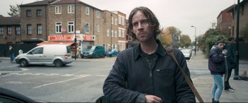 Movie still from “A Street Cat Named Bob” (2016), directed by Roger Spottiswoode – A man standing on the side of the street; Medium shot, Over the shoulder angle