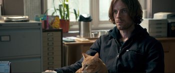 Movie still from “A Street Cat Named Bob” (2016), directed by Roger Spottiswoode – A man sitting next to a cat in a room; Medium shot, Over the shoulder angle