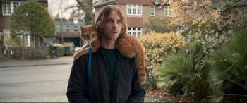 Movie still from “A Street Cat Named Bob” (2016), directed by Roger Spottiswoode – A man holding a cat on his shoulder; Medium shot, Over the shoulder angle